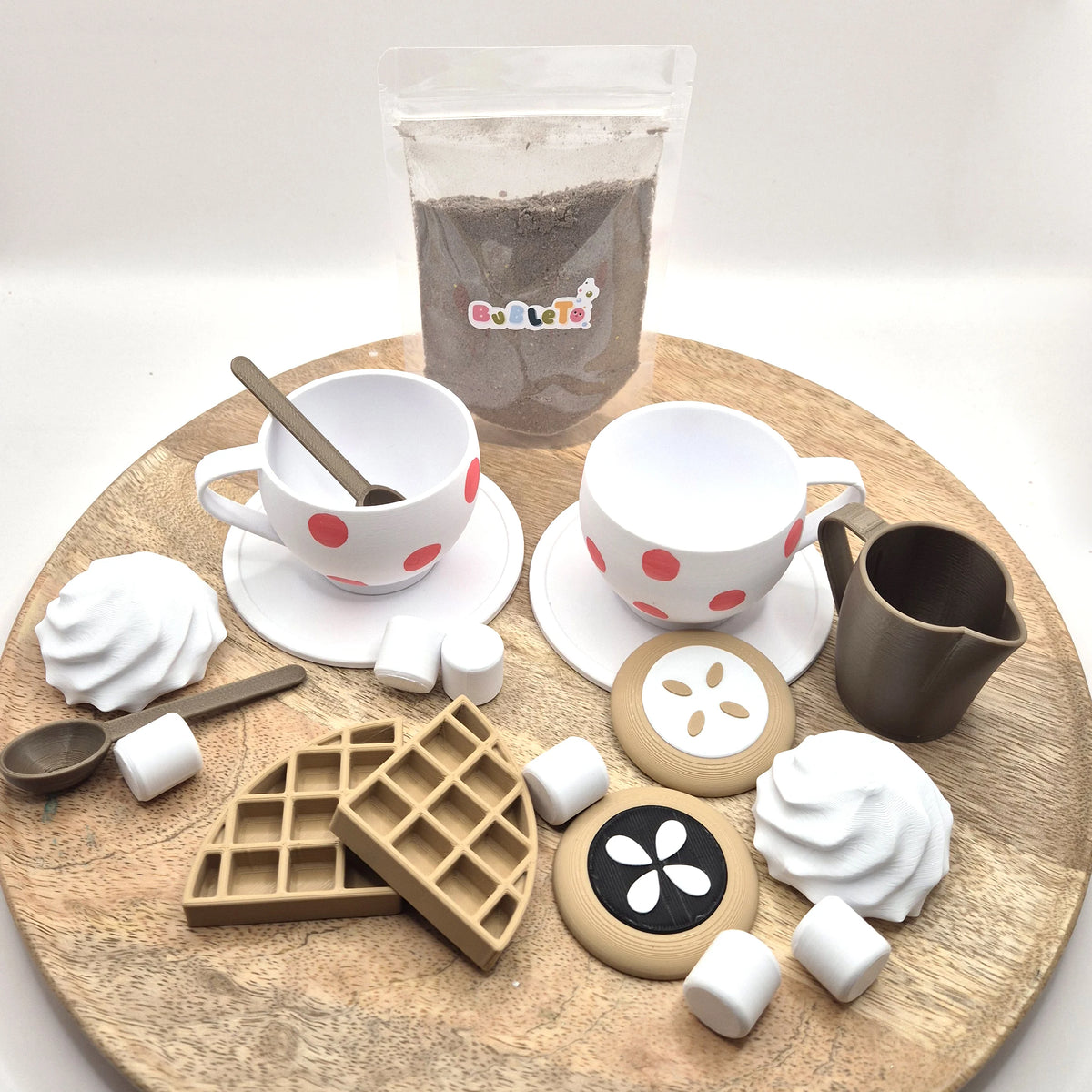 Šálky s bodkami, mliekovka, vafle, koláčiky a marshmallow z 3D tlače, za nimi priehľadné vrecko prášku BubleTo